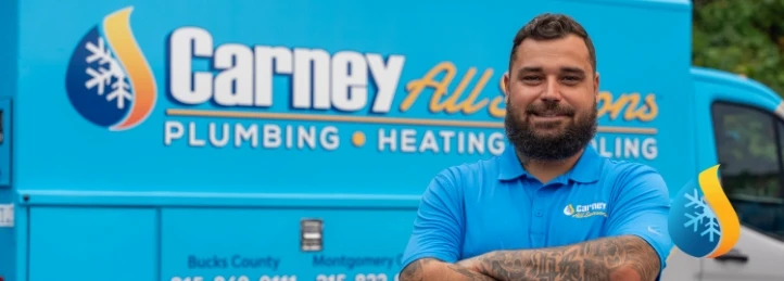 Bearded technician with arms crossed in front of Carney All Seasons plumbing, heating, and cooling service van.